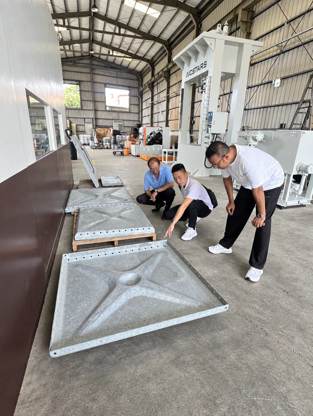 VICSTARS team and visitors reviewing formed parts beside production equipment during a factory discussion
